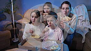 Big family watching late night TV show or movie on sofa and eating pizza and popcorn
