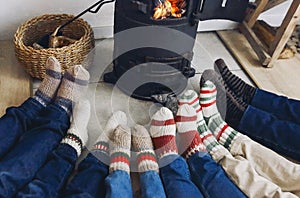 Big family wearing warm woolen socks warming feet by fireplace at cozy home in winter time