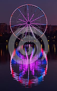 Big ferris wheel at night. Colorful reflection on the lake.