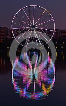 Big ferris wheel at night. Colorful reflection on the lake.