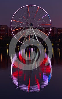 Big ferris wheel at night. Colorful reflection on the lake.