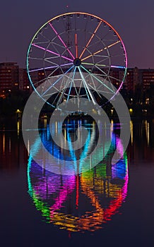 Big ferris wheel at night. Colorful reflection on the lake.