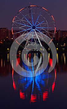 Big ferris wheel at night. Colorful reflection on the lake.