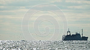 Big fishing boat trawling and catching fish as it crosses sea at horizon line during sunset. the fishing and sea-faring