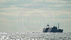 Big fishing boat trawling and catching fish as it crosses sea at horizon line during sunset. the fishing and sea-faring