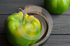 Big fresh organic green bell pepper in wooden plate on dark wooden table background, copy space