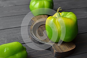 Big fresh organic green peppers in wooden plate over dark wooden background