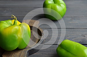 Big fresh organic green peppers in wooden plate over dark wooden background