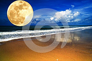 Big full yellow moon in dark blue cloudy sky over the sea / ocean. Empty beach. Planet close to the Earth.