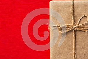 Big gift box wrapped in brown Kraft paper tied with twine on crimson red textured background. Trendy Christmas New Years card