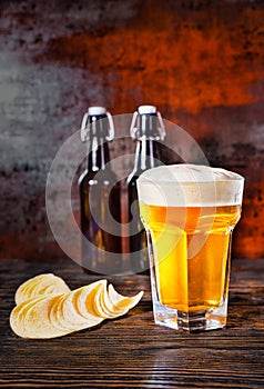 Big glass of freshly poured light beer against two beer bottles