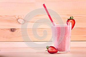 A big glass full of appetizing smoothie. A berry shake on a wooden background. Tasty milkshake with a straw and cut strawberries.