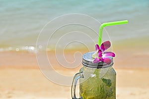 Big glass of mojito with orchid flower on beach