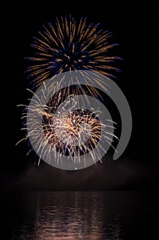 Big gold and blue stars from fireworks over Brno`s Dam with lake reflection