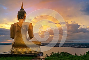 The big golden Buddha statue of Phu Salao temple with Mekong River flows through the Pakse city in beautiful sunset moment at Paks