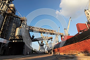 Big grain terminal at seaport. Cereals bulk transshipment from road transport to vessel. Loading grain crops on ship photo