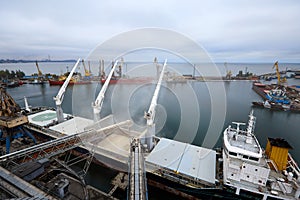 Big grain terminal at seaport. Cereals bulk transshipment from road transport to vessel. Loading grain crops on bulk