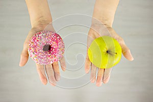 Big green apple and pink doughnut in hand. The concept of diet comparison