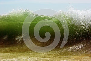 A big green beachbreak wave against blue sky