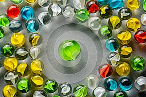 A big green glass marble  between yellow, green, blue and red marbles on a table
