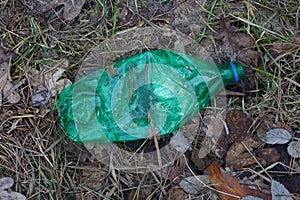 Big green plastic bottle lying on brown earth and needles