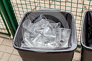 Big grey trach can full of used plastic transparent cups. Environment and world ocean pollution with plastic waste. Recycling mate