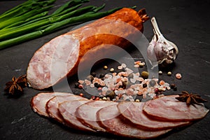 Big half of smoked ham sausage with sliced pieces, garlic and onion