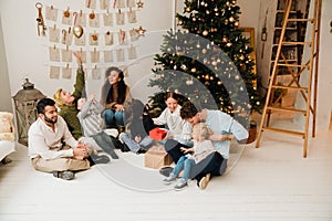 Big happy family exchanging gifts while sitting on floor near Christmas tree at home