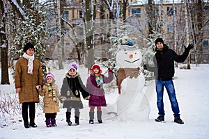 Big happy family: father, daughters and grandmother sculpt a big real snowman