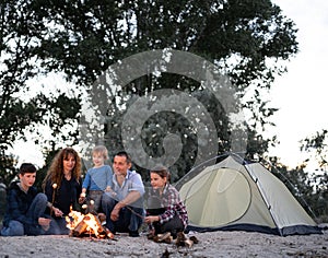 Big happy family of five people, dad, mom, sons and daughter are sitting around the fire roasting marshmallows and enjoy