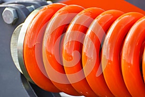 Big and hard orange steel spring as part and detail of industrial or agricultural machine