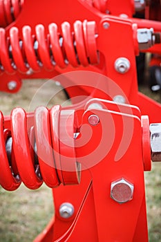 Big and hard red steel spring as part and detail of industrial or agricultural machine