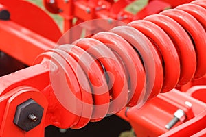 Big and hard red steel spring as part and detail of industrial or agricultural machine