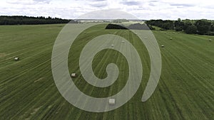 Big hay bale rolls on a green field with blue sky and clouds on the background. Shot. Rural landscape with mowed grass