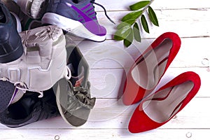 Big heap of different sports shoes and red high heel women`s shoes on white background.