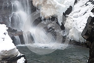 Big high Waterfall in the mountain winter forest with snow-covered trees and snowfall