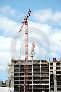 Big hoisting tower cranes and top section of modern construction building in a city over blue sky with clouds