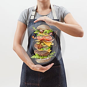 Big homemade fresh burger in the girl`s hands from flying ingredients - fresh vegetables and organic natural beef meat