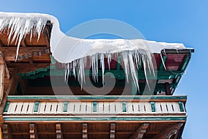 Big icicles and snow hanging over the rain gutter on a roof of a traditional wooden house in the mountains in winter.