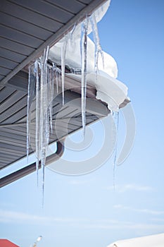 Big icicles on the roof of a house on a snowy winter day. Thaw.