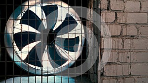 Big industrial fan in a white brick wall of a factory.