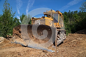 Big industrial yellow bulldozer leveling ground on road construction