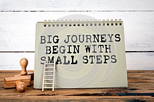Big Journeys Begin With Small Steps. Green notepad on wooden texture table and white background