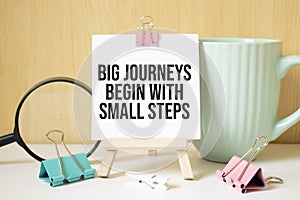 Big journeys begin with small steps text written on black notebook with magnifying glass and a pen. Business and achievement