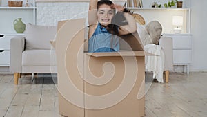 Big large cardboard box package stands on floor in interior of living room near sofa unexpectedly happy little girl