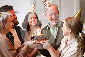 Big lovely caucasian family in party hats congratulating happy senior grandfather with his birthday