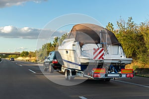 Big luxury cabin motorboat cruiser yacht trailer SUV carrier go to river lake on highway road sunset summer light