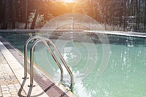 Big luxury empty rectangular swimming pool with clean blue water and ladder at tropical forest beach resort at sunrise