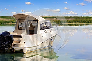 Big luxury fishing boat with cabin moored near river or lake shore in still water. Blue sky on the background. Summer adventure,