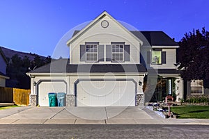 Big luxury house with triple garage doors at dusk, night in suburbs